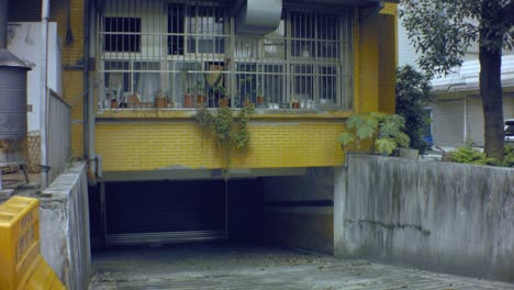 vertical-looking-up-view-from-a-dirty-old-cement-paved-underground-garage-with-closed-metal-gate-up-to-ghetto-like-dirty-bared-window-chimney-structure-two-story-high-building-with-yellow-tiled-wall