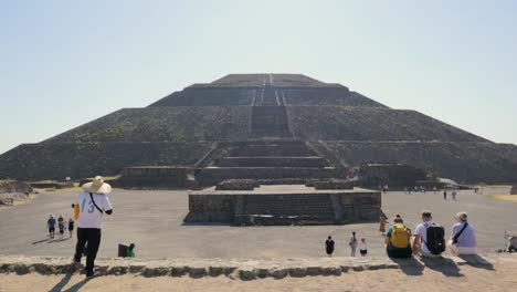 Wide,-handheld-shot-of-tourists-looking-at-the-ancient-pyramid-of-the-sun-at-the-archaeological-site-of-Teotihuacan-in-Mexico,-on-a-clear,-sunny-day