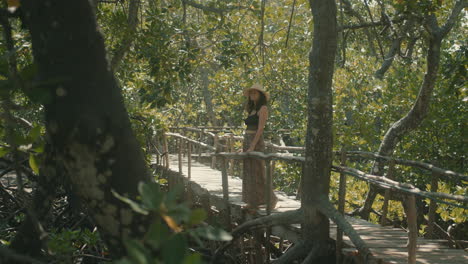 Slow-motion-of-an-attractive-Caucasian-woman-wearing-a-straw-hat-looking-out-and-enjoying-the-forest-from-a-wooden-bridge