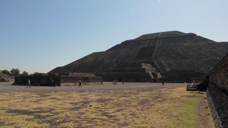 A-wide-dolly-in-slow-motion-shot-of-the-Pyramid-of-the-Sun-at-the-Teotihuacan-archaeological-site-in-Mexico,-with-some-tourists-walking-around-and-the-blue-sky-on-a-clear-and-sunny-day