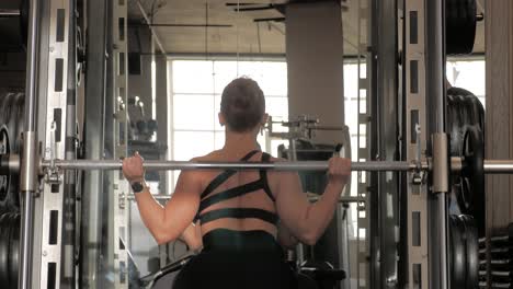 One-woman-making-squats-at-the-gym-with-the-dead-weight-bar,-seen-from-behind,-unrecognizable-person