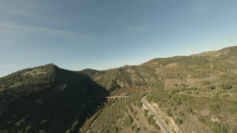 Luftaufnahme-Der-Trockenen-Olivenhainhügel-Und-Der-Alten-Bogenbrücke-In-Spanien