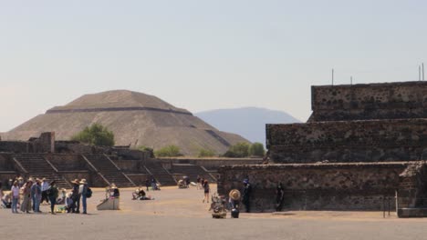 A-wide-tracking-shot-of-the-archaeological-zone-of-Teotihuacan-in-Mexico,-with-the-Pyramid-of-the-Sun-and-other-ruins-in-the-background,-on-a-clear-and-sunny-day-with-tourists-walking-around