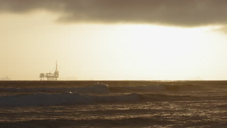 Slow-Motion-waves-crashing-with-an-oil-rig-in-the-background-at-sunset