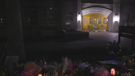 Berkey-Hall-on-the-campus-of-Michigan-State-University,-the-site-of-a-mass-shooting-in-February-of-2023-at-night-with-flower-memorial-panning-left-to-right