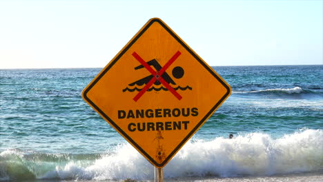 A-man-swims-in-front-of-a-dangerous-current-sign-at-Bondi-Beach,-Sydney-Australia