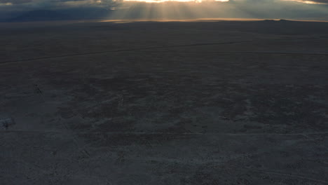 Aerial-panning-up-across-desert-landscape-to-sunrise-god-rays-through-clouds