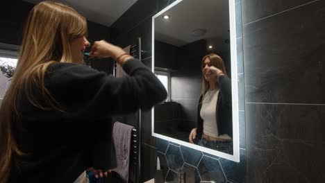 Weibliches-Model-Schaut-In-Einen-Badezimmerspiegel-Mit-Hintergrundbeleuchtung-Und-Wäscht-Sich-Die-Zähne