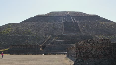 A-tracking-shot-of-the-Pyramid-of-the-Sun-in-the-archaeological-zone-of-Teotihuacan-in-Mexico,-with-some-tourists-walking-around-it-on-a-clear-and-sunny-day