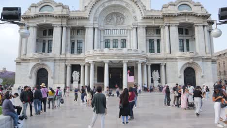 A-wide-slow-motion-dolly-in-shot-of-people-walking-outside-the-Palacio-de-Bellas-Artes-in-Mexico-City,-on-a-clear-day-with-blue-sky