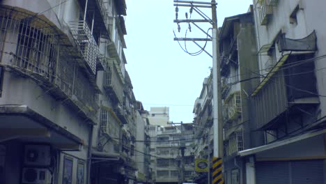 Taipei,-Taiwan---Jan-28th-2019:-look-up-vertical-view-of-ghetto-old-dirty-asia-apartment-building-in-an-alley-cars-with-electricity-poles-and-cables-hanging-across-in-sky-and-all-bared-window-balcony