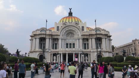 A-wide-dolly-in-and-slow-motion-shot-of-the-Palacio-de-Bellas-Artes-in-Mexico-City-with-some-people-walking-around,-on-a-clear-afternoon-with-a-blue-sky