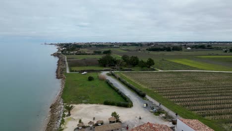 People-ride-bicycles-near-farmland-at-the-village-of-Loix-in-Île-de-Ré-Island-in-Western-France,-Aerial-flyover-shot