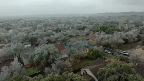 Frozen-icy-trees-in-Austin-Texas-suburban-neighborhood-during-cold-winter-freeze,-aerial-drone-orbit-and-pan-right-over-South-Austin-homes