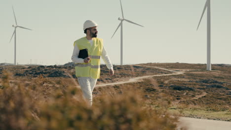 A-male-Caucasian-renewable-energy-expert-in-safety-gear-inspects-wind-turbines-while-walking,-symbolizing-our-commitment-to-clean-energy