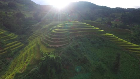 Rice-field-terraces-in-the-mountains,-scenic-drone-landscape-with-a-sunburst-in-the-background,-no-people