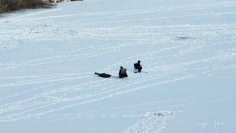 Eisfischer-Sitzen-über-Einem-Loch-In-Boseman-Montana-Auf-Einem-Zugefrorenen,-Verschneiten-Vorstadtteich-Und-Kreisen-Während-Der-Goldenen-Stunde-Mit-Einer-4K-Teledrohne-Nach-Rechts