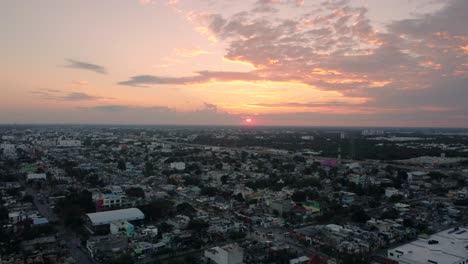Aerial-view-of-a-town-and-behind-there's-a-beautiful-sunset-that-paints-the-sky-with-bright-warm-tones,-Playa-del-Carmen