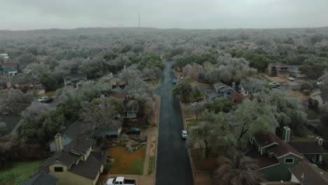 Frozen-icy-trees-in-Austin-Texas-suburban-neighborhood-during-cold-winter-freeze,-aerial-flyover-street-and-tilt-up-over-Oak-Hill-homes