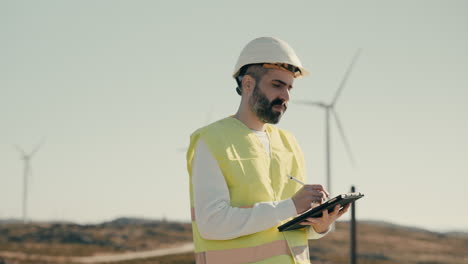 A-focused-Caucasian-male-engineer-in-a-reflective-vest-uses-cutting-edge-technology-to-ensure-the-efficiency-of-wind-turbines,-promoting-clean-energy-production