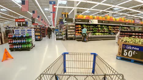 Pushing-an-emptying-grocery-cart-towards-the-produce-section-in-a-large-American-grocery-story