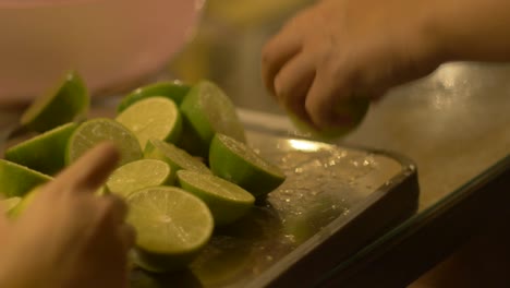 Freshly-picked-green-limes-being-cut-into-half-on-wooden-chopping-board,-filmed-as-close-up-shot