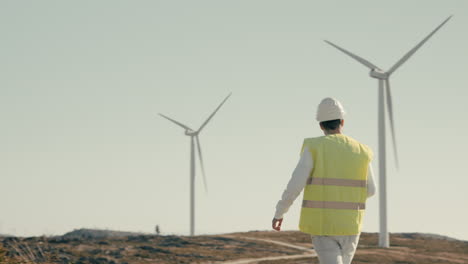 Wide-shot-of-a-renewable-energy-engineer-walking-and-checking-wind-turbines,-symbolizing-the-importance-of-sustainable-energy-for-our-planet's-future