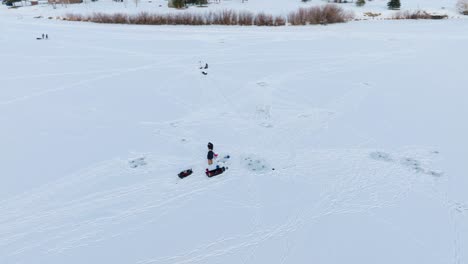 Boseman-Montana-ice-fishermen-on-snowy-frozen-suburban-pond,-tracking-right-with-4k-drone-during-golden-hour