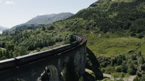 Drohnenaufnahme,-Die-Einem-Zug-Auf-Dem-Historischen-Glenfinnan-Viadukt-In-Schottland-Folgt