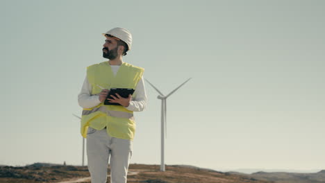 Medium-shot-of-a-focused-young-Caucasian-male-engineer-using-a-tablet-to-audit-wind-turbines,-showcasing-the-use-of-technology-to-support-sustainable-energy