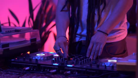 DJ-with-dreadlocks-remixing-music-using-turntable-during-live-performance,-filmed-as-close-up-on-lower-body