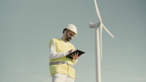 Renewable-energy-engineer-uses-a-tablet-to-audit-wind-turbines-in-a-field-of-clean-energy-generators-on-a-sunny-day,-working-to-save-planet-earth