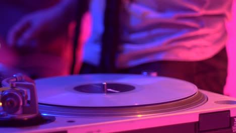 Vinyl-scratched-on-turntable-during-live-performance-with-warm-pink-and-blue-lighting-setup,-filmed-as-close-up-on-hand-motion
