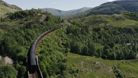 Drohnenaufnahme-Des-Hogwarts-Express,-Der-Durch-Die-Grüne-Landschaft-Schottlands-Fährt
