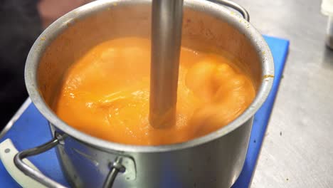 Close-up-of-orange-cream-sauce-being-whipped-in-a-hot-pot-with-smoke-coming-out-of-it