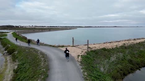 Family-riding-bicycles-near-shore-with-toddler-riding-on-Father's-bike,-Aerial-follow-behind-shot