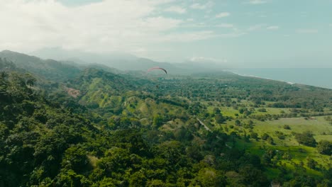 Aerial-shot-chasing-a-paragliding-flying-towards-the-mountains-and-sea,-Colombia,-la-guajira