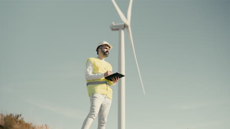 Eco-conscious-engineer-checks-wind-turbines-in-a-field-of-renewable-energy-generators,-using-technology-on-tablet-to-ensure-a-sustainable-future