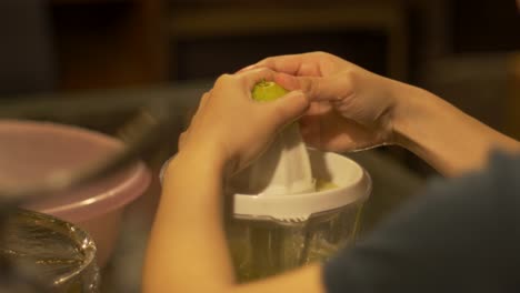 Lime-juice-being-extracted-from-fresh-green-limes-by-electric-citrus-juicer,-filmed-over-left-shoulder-as-medium-close-up-shot