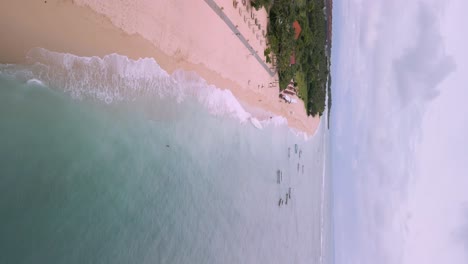 Vertical-drone-shot-of-waves-rooling-from-the-clear-blue-sea-on-Geger-beach-in-Bali