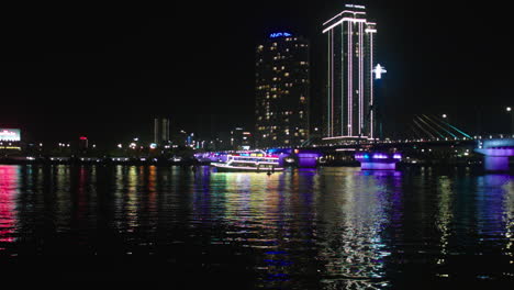 Nachtansicht-Der-Tran-Thi-Ly-Brücke-über-Den-Han-Fluss-Und-Kreuzfahrtschiff-In-Der-Vietnamesischen-Stadt-Da-Nang,-Beleuchtet-Mit-Lichtern-Und-Skyline-Gebäuden-Im-Hintergrund