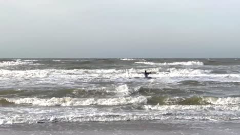 Surfer-with-kite-jumping-over-large-waves-during-cloudy-day-in-Netherlands---Wide-shot