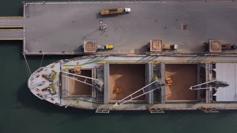 Aerial-view-of-a-cargo-ship-full-of-wheat-unloading-its-cargo-onto-cargo-trucks-at-a-commercial-dock