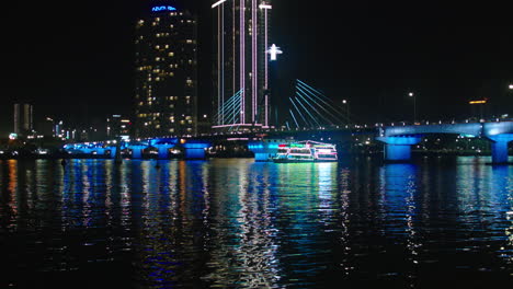 Filmische-Nachtansicht-Der-Tran-Thi-Ly-Brücke-über-Den-Han-Fluss-Und-Kreuzfahrtschiff-In-Der-Vietnamesischen-Stadt-Da-Nang,-Beleuchtet-Mit-Lichtern-Und-Skyline-Gebäuden-Im-Hintergrund