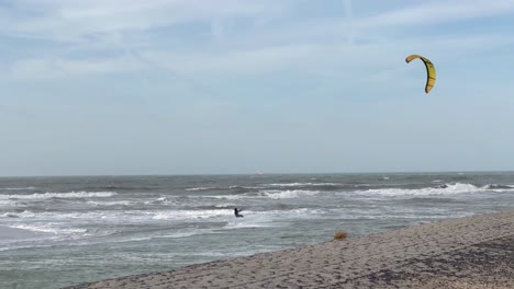 Wide-shot-of-kite-surfer-speeding-on-large-waves-of-North-Sea-during-cloudy-day