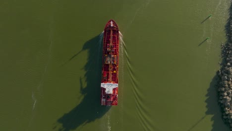 Top-view:-A-red-cargo-ship-floats-in-murky-green-water