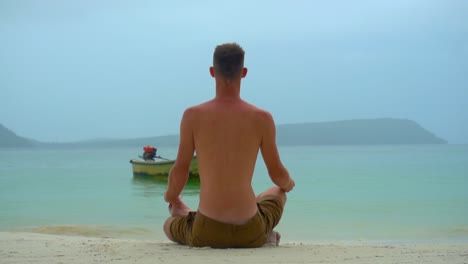 Man-sat-on-tropical-beach,-meditating,-with-beautiful-view-out-to-sea