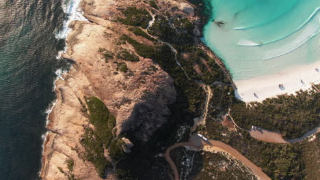 High-altitude-top-down-drone-trucking-shot-cliffs-and-rocks-next-to-a-beautiful-white-beach-in-Australia