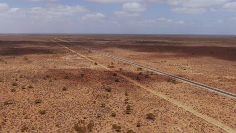Drone-zoom-out-of-campervan-on-empty-road-surrounded-by-dry-landscape-of-Australia---Nullarbor