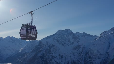 Camera-following-the-ascent-of-an-empty-cable-car-to-a-ski-slope-on-top-of-snow-capped-mountains-on-a-sunny-day